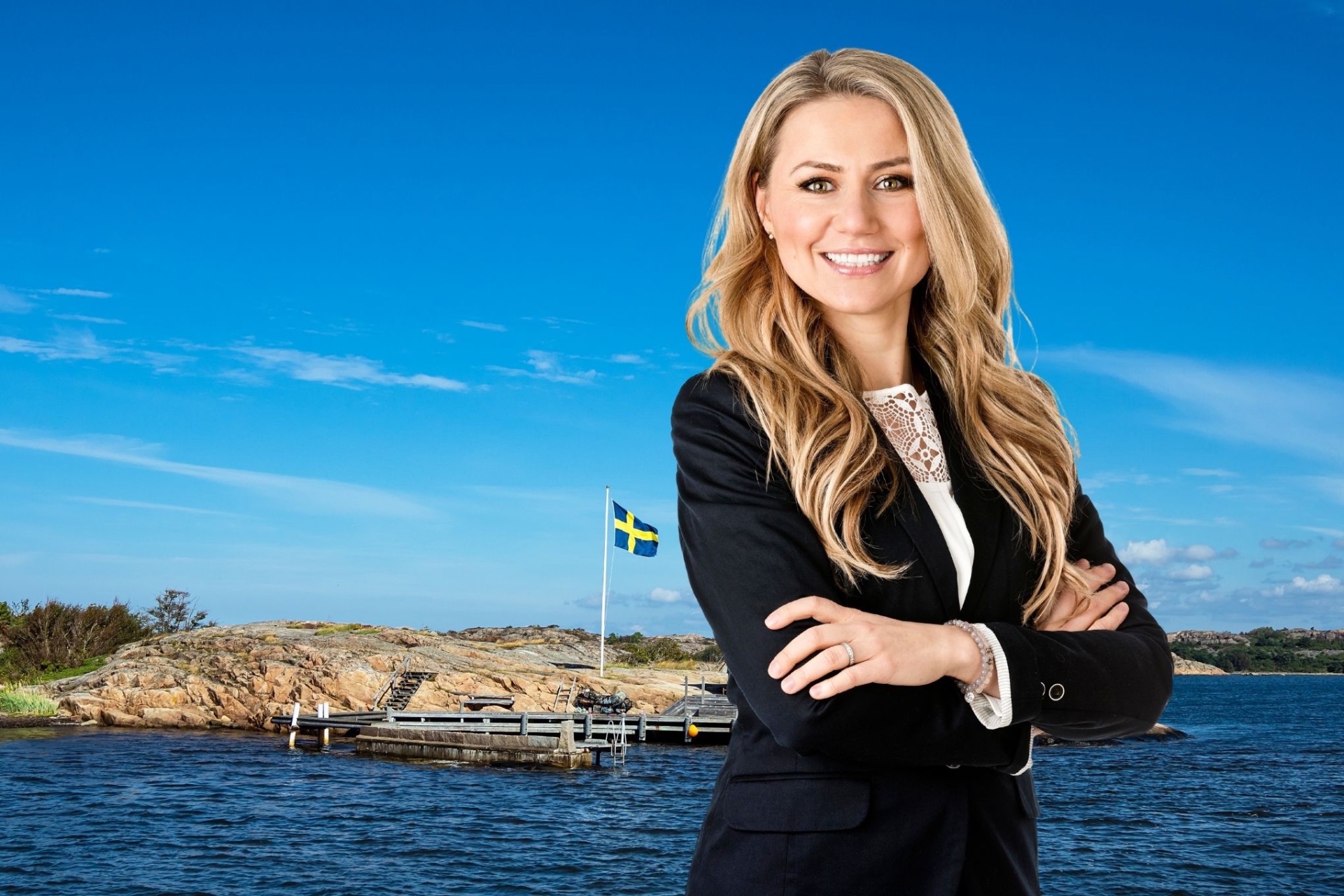 Leende kvinna i kavaj står med armarna i kors framför havsvik och klippig ljunghed. strandskyddsjurist Giedre Jirvell
